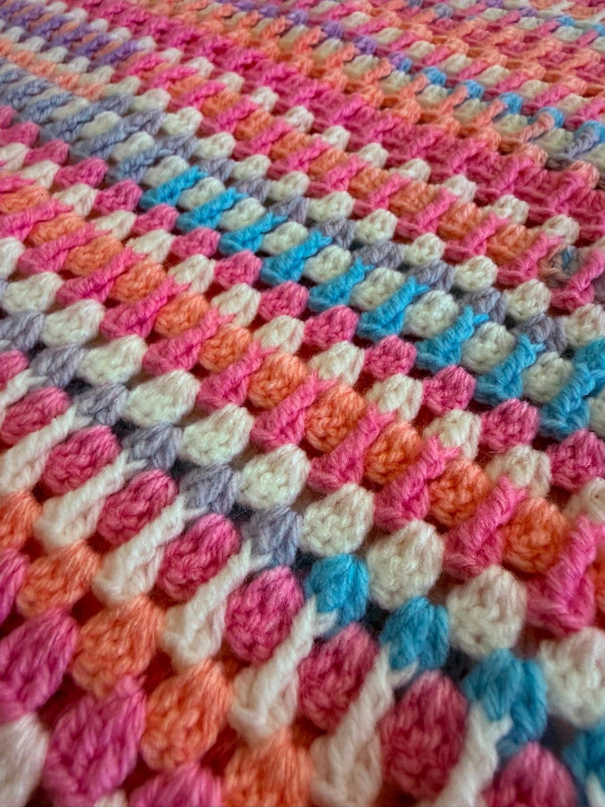Close-up of the multicolour crochet cardigan showing the pink, turquoise, blue, green and white stitch rows in premium acrylic yarn.