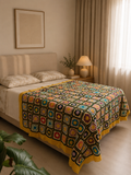 Large handmade multicolour floral motif crochet blanket displayed across a bed with contrasting dark joins and yellow borders.