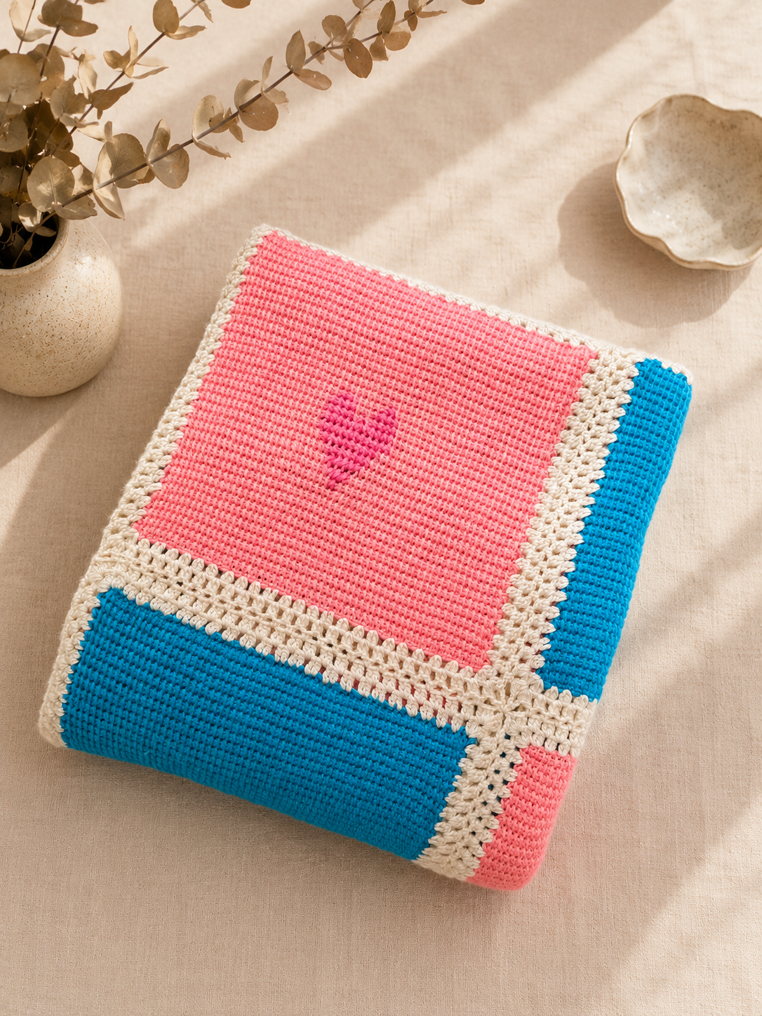 Folded multicolour Tunisian crochet blanket showing pink and turquoise panels, cream joins and embroidered heart details.