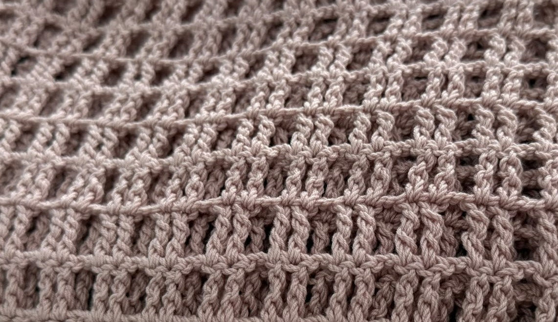 Close-up of the square openwork crochet stitches worked in dusty mauve KnitMe Vegan acrylic yarn.