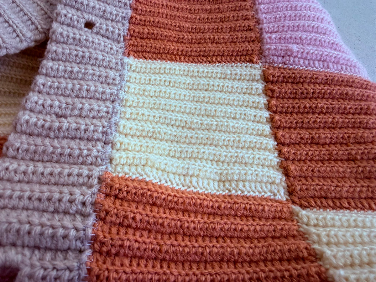 Close-up of the patchwork crochet cardigan showing the striped block texture and decorative topstitching over selected joins.