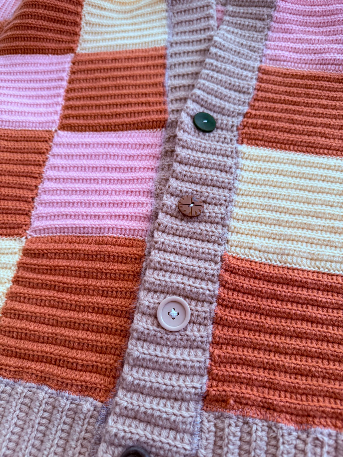 Close-up of the crochet cardigan front placket showing assorted buttons in different colours and types.
