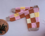 Folded diagonal view of the multicolour crochet cardigan showing the patchwork sleeves, front opening and ribbed cuffs.