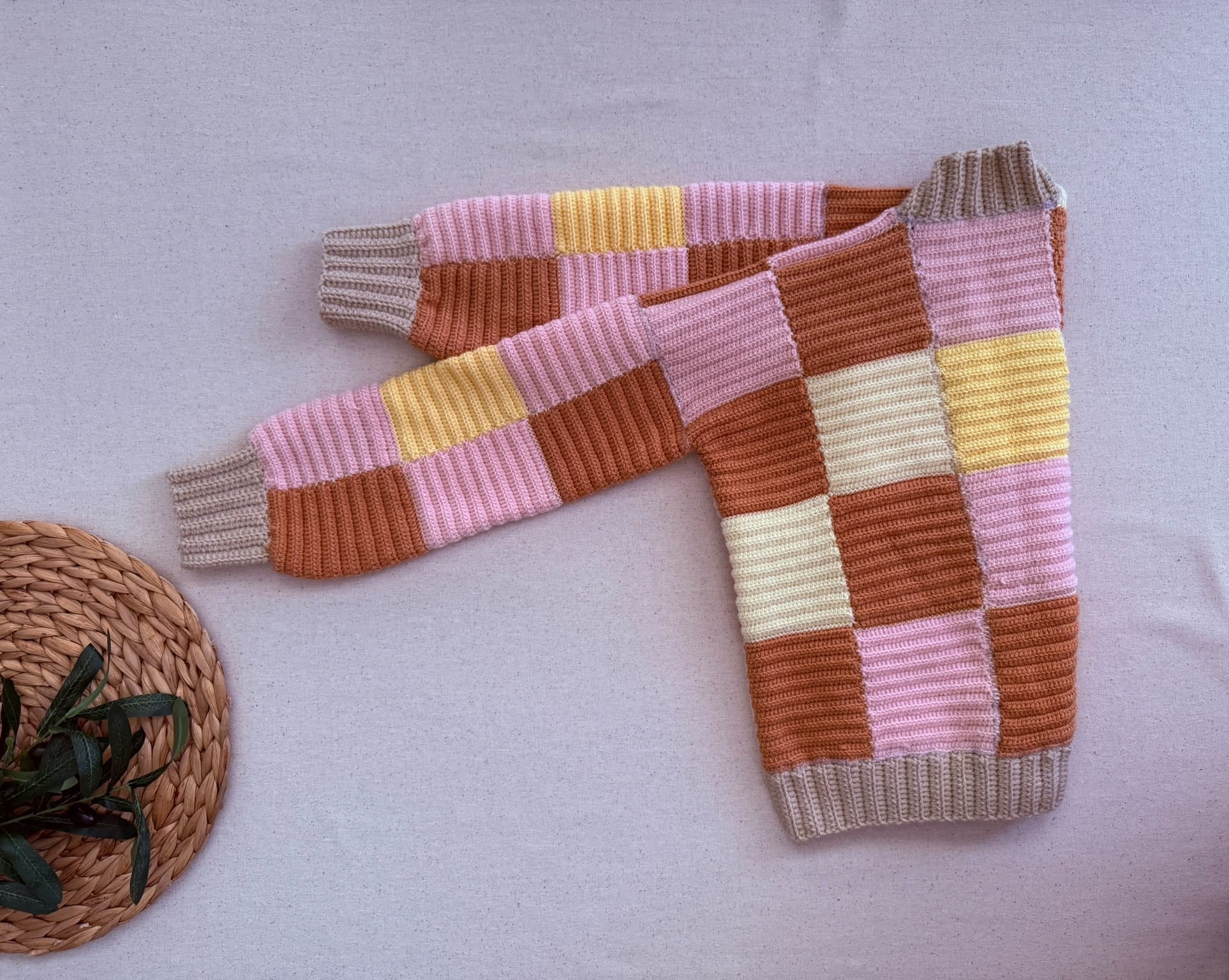 Folded diagonal view of the multicolour crochet cardigan showing the patchwork sleeves, front opening and ribbed cuffs.