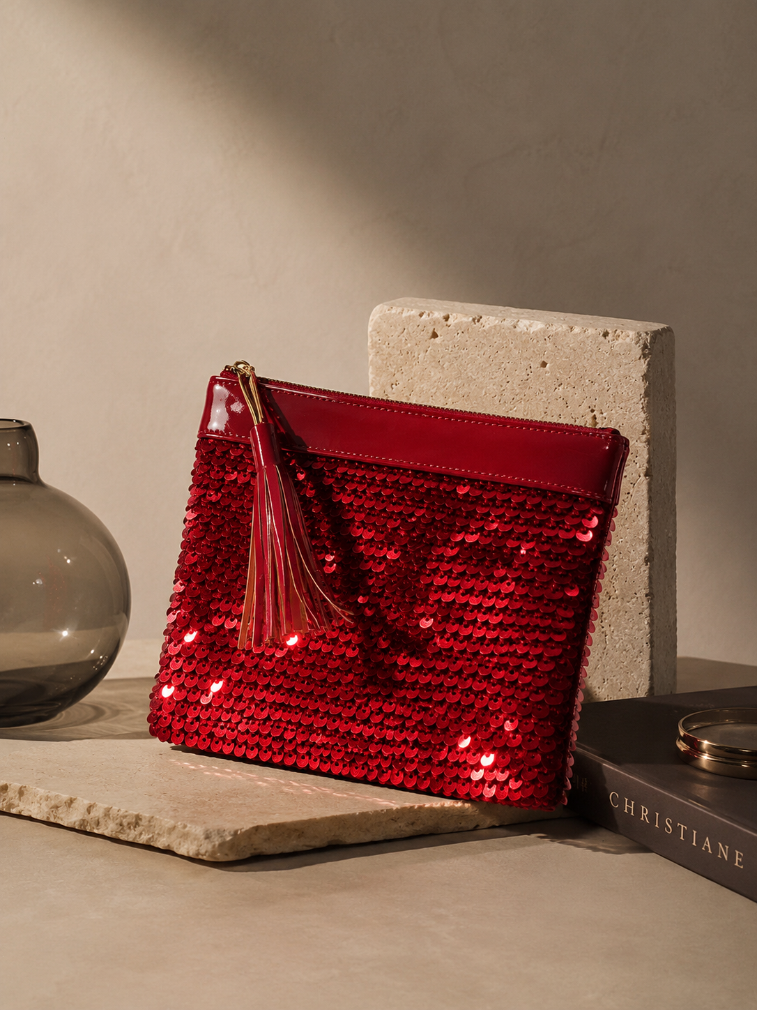 Angled view of the handmade red sequin clutch bag showing its sequined surface and tassel detail.
