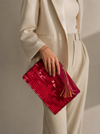 Handmade red sequin clutch bag held by hand, shown from the front with patent leather tassel detail.