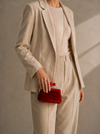 Handmade red sequin clutch bag carried by hand with a neutral tailored outfit, showing its compact shape and kiss-lock closure.