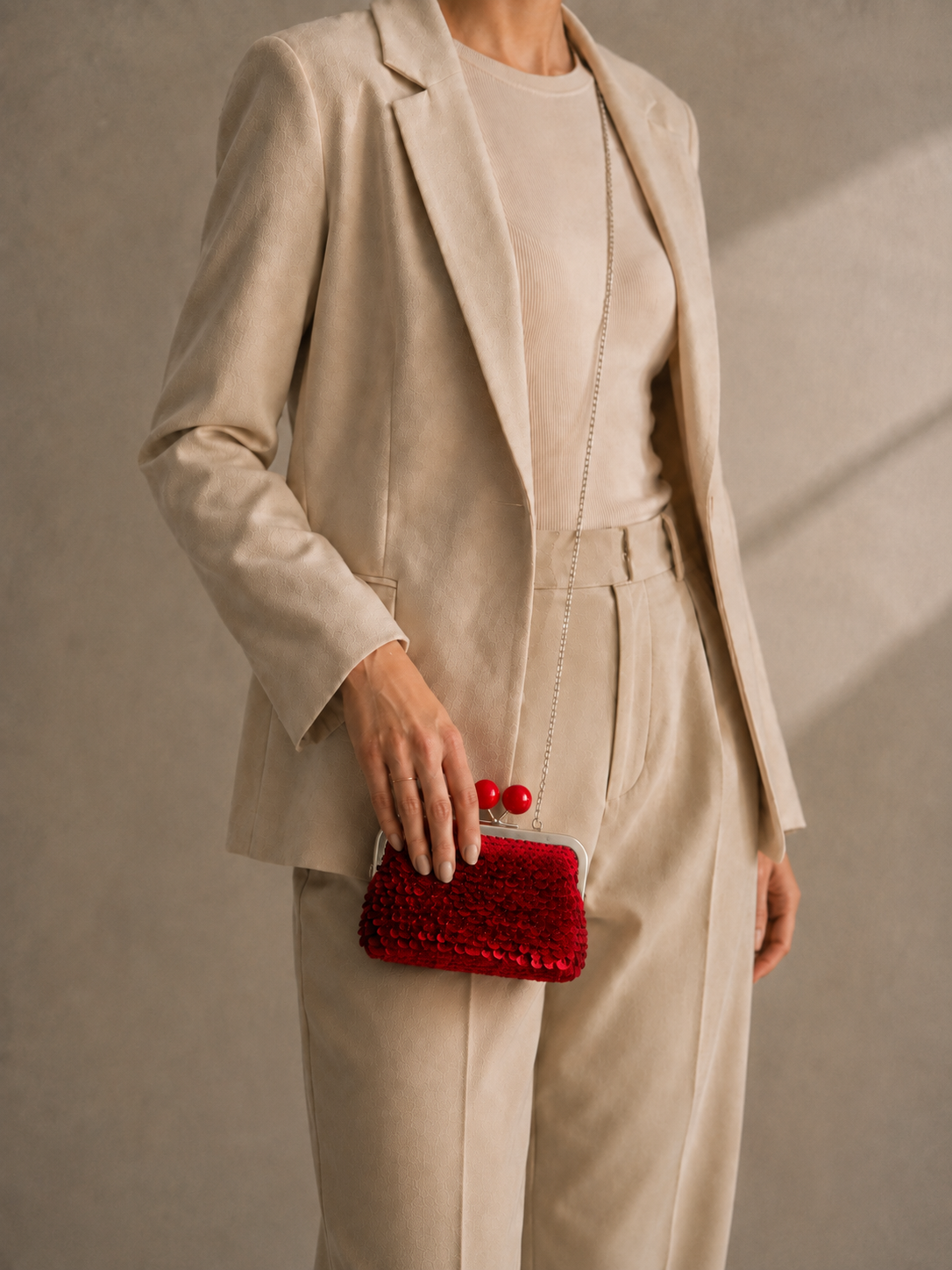 Handmade red sequin clutch bag carried by hand with a neutral tailored outfit, showing its compact shape and kiss-lock closure.