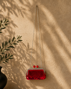 Small red sequin evening purse displayed with its silver chain against a warm neutral background with botanical shadows.