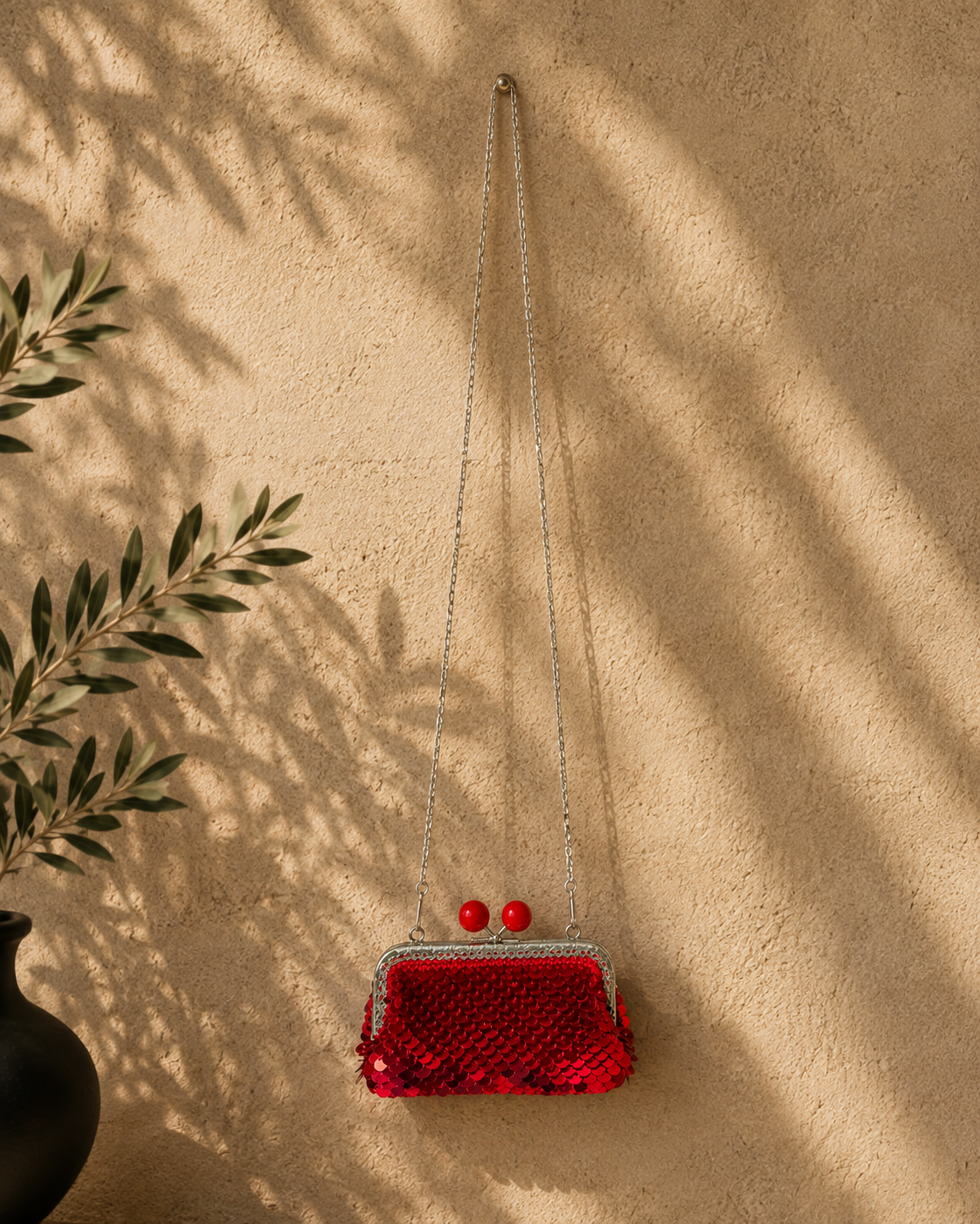 Small red sequin evening purse displayed with its silver chain against a warm neutral background with botanical shadows.