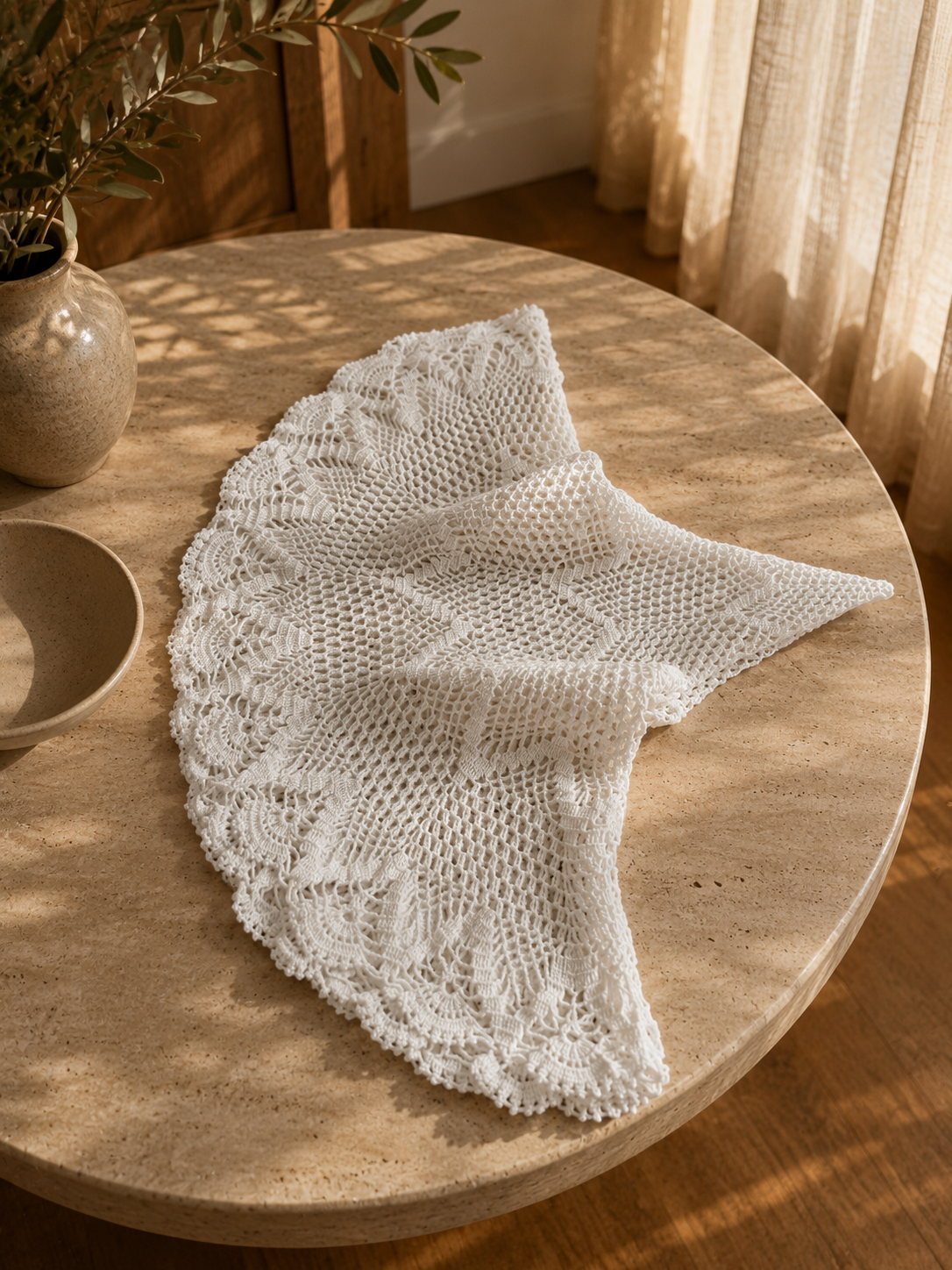 Overhead view of the round white crochet lace table topper partially opened on a circular wooden table.