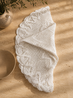 Partially folded white crochet lace table topper showing the depth and movement of its decorative scalloped border.