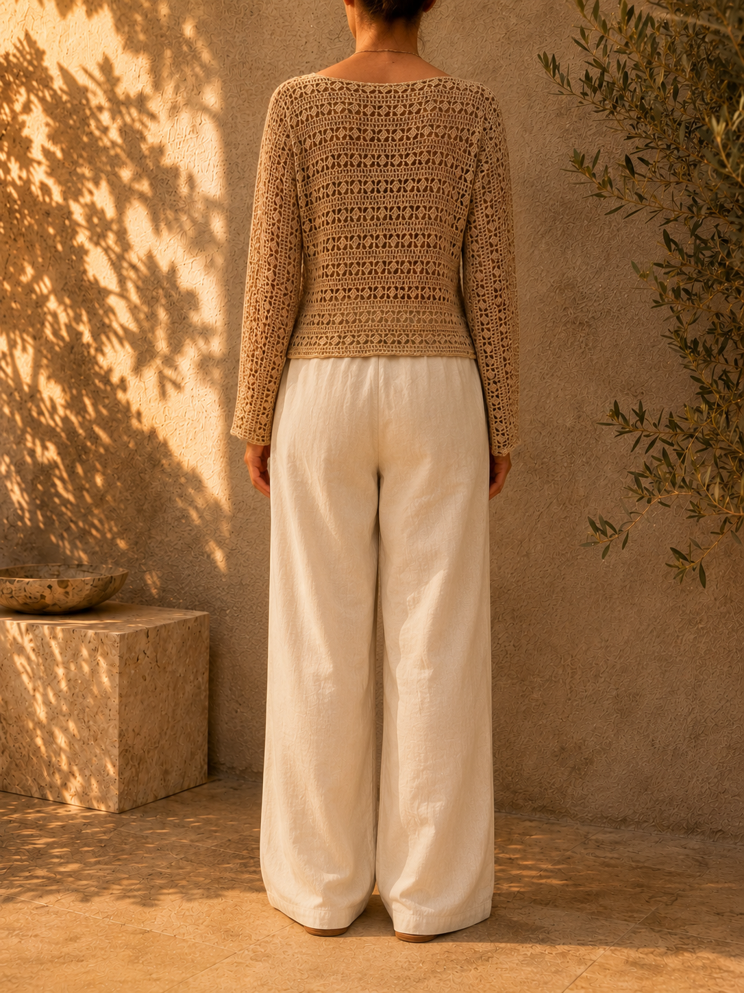 Back view of the sand-beige crochet blouse showing the repeating openwork pattern across the body and long sleeves.
