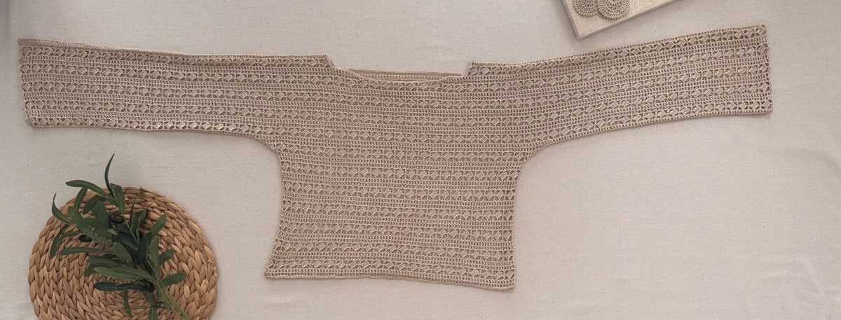 Flat-lay view of the sand-beige crochet blouse showing its broad cuff-to-cuff construction, wide shallow neckline and waist-length body.