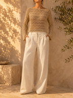 Front view of the handmade sand-beige crochet blouse styled with ivory wide-leg trousers, showing its wide neckline and long openwork sleeves.