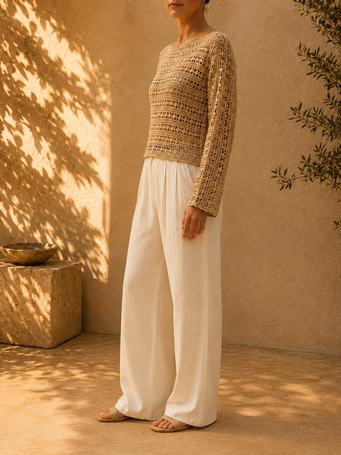 Side view of the handmade sand-beige crochet blouse showing its relaxed long sleeve and softly structured waist-length silhouette.