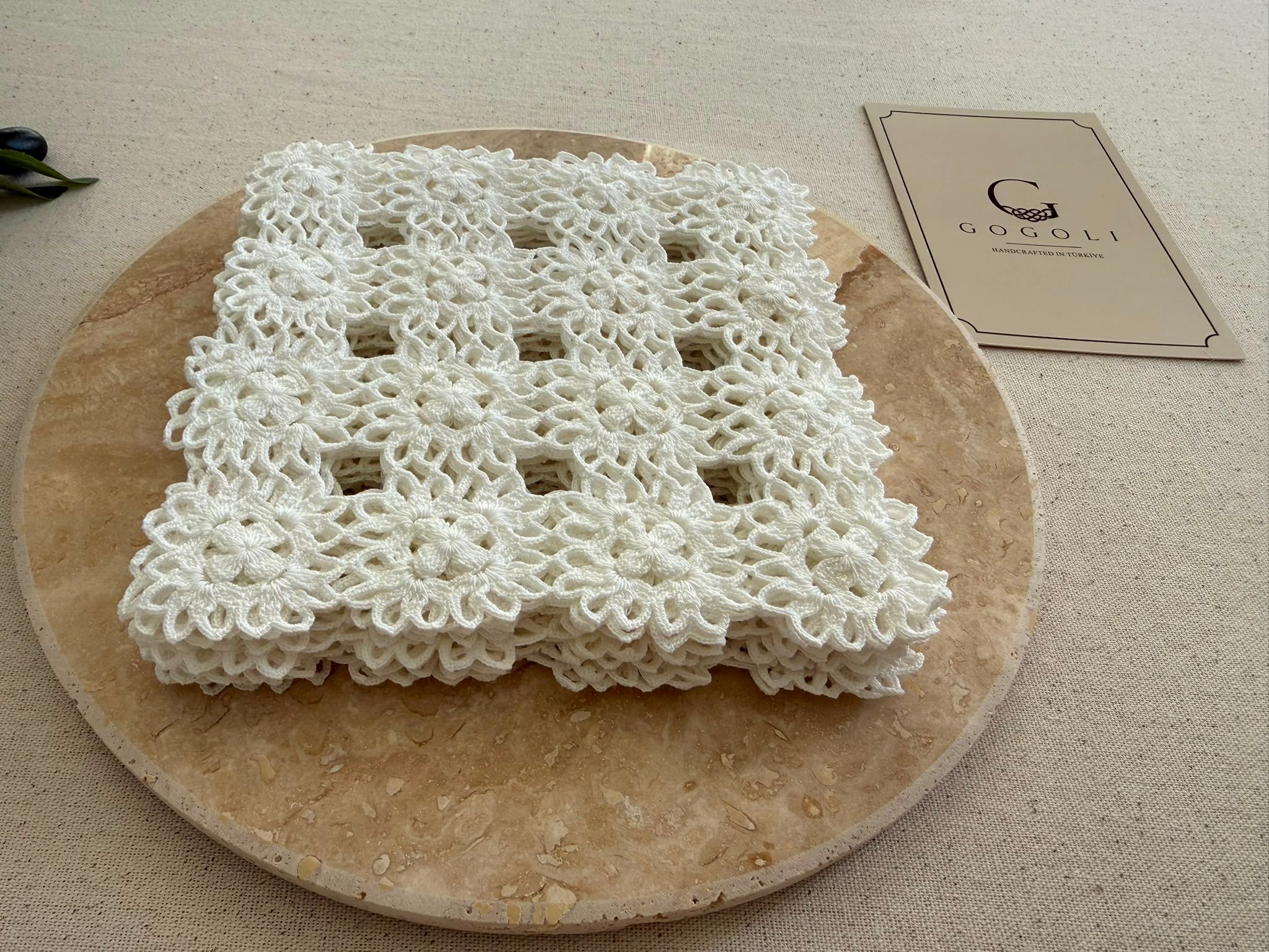 Small square white crochet doily displayed on a neutral stone surface, showing its compact four-by-four motif construction.