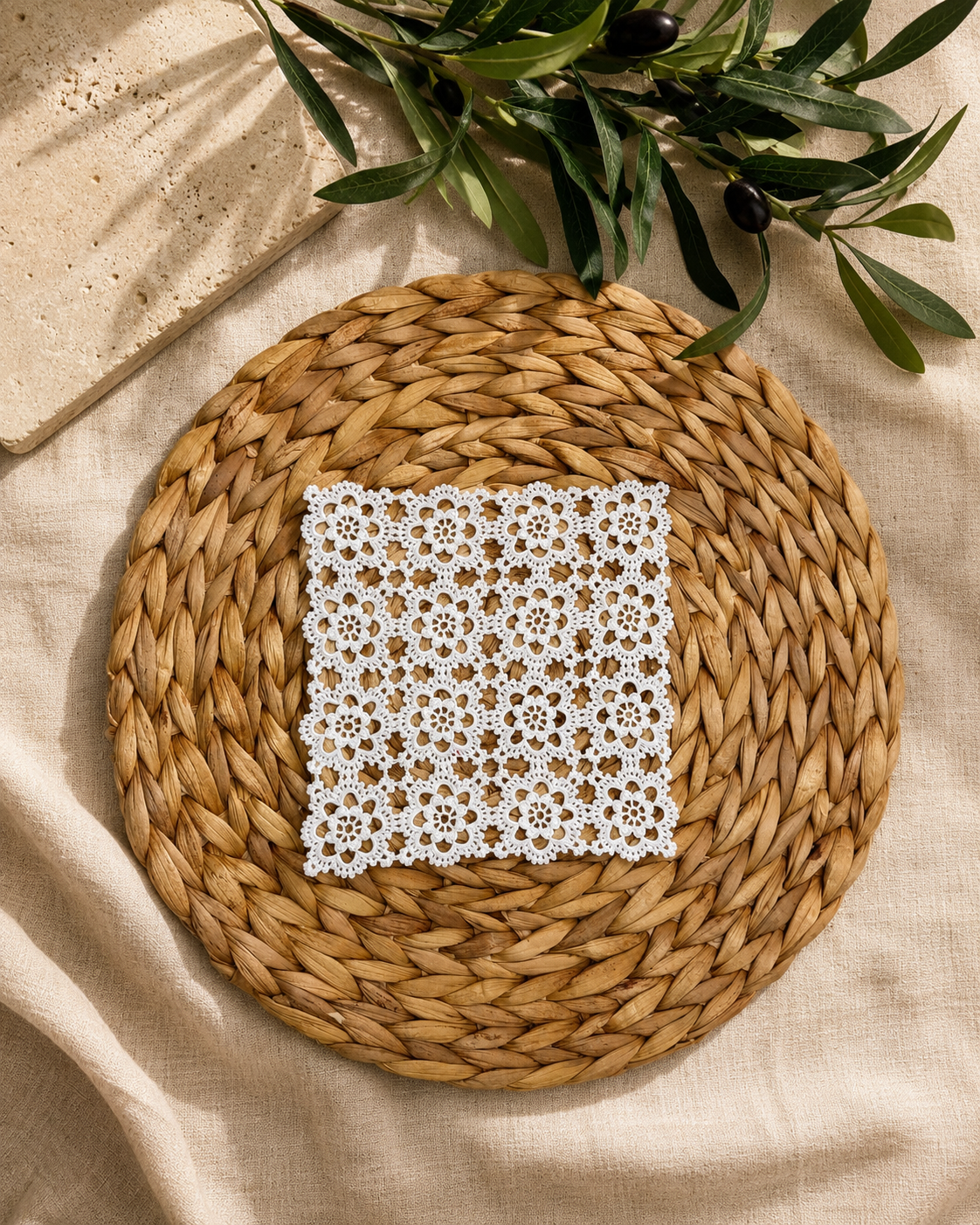 Small square white crochet doily displayed on a round woven mat, showing its four-by-four floral motif construction.