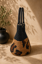 Side profile of the structured paper yarn handbag showing its tapered crochet body, rigid handles and oval-base construction.