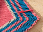 Close-up of the multicolour striped crochet border with a crochet hook resting on the handmade blanket.
