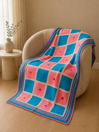 Large handmade Tunisian crochet blanket draped over a chair, showing its graphic panel layout and striped border.