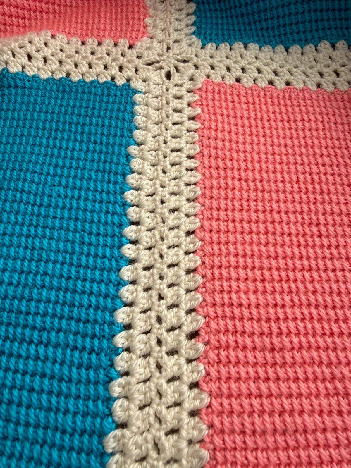Close-up of turquoise and pink Tunisian crochet panels joined by hand with textured cream crochet lines.