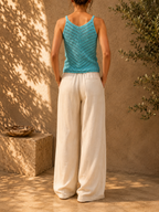 Back view of the handmade turquoise crochet tank top styled with light trousers, showing the sleeveless silhouette and crochet construction.