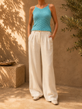Front view of the handmade turquoise crochet tank top styled with ivory wide-leg trousers, showing its V-neck and diagonal openwork design.