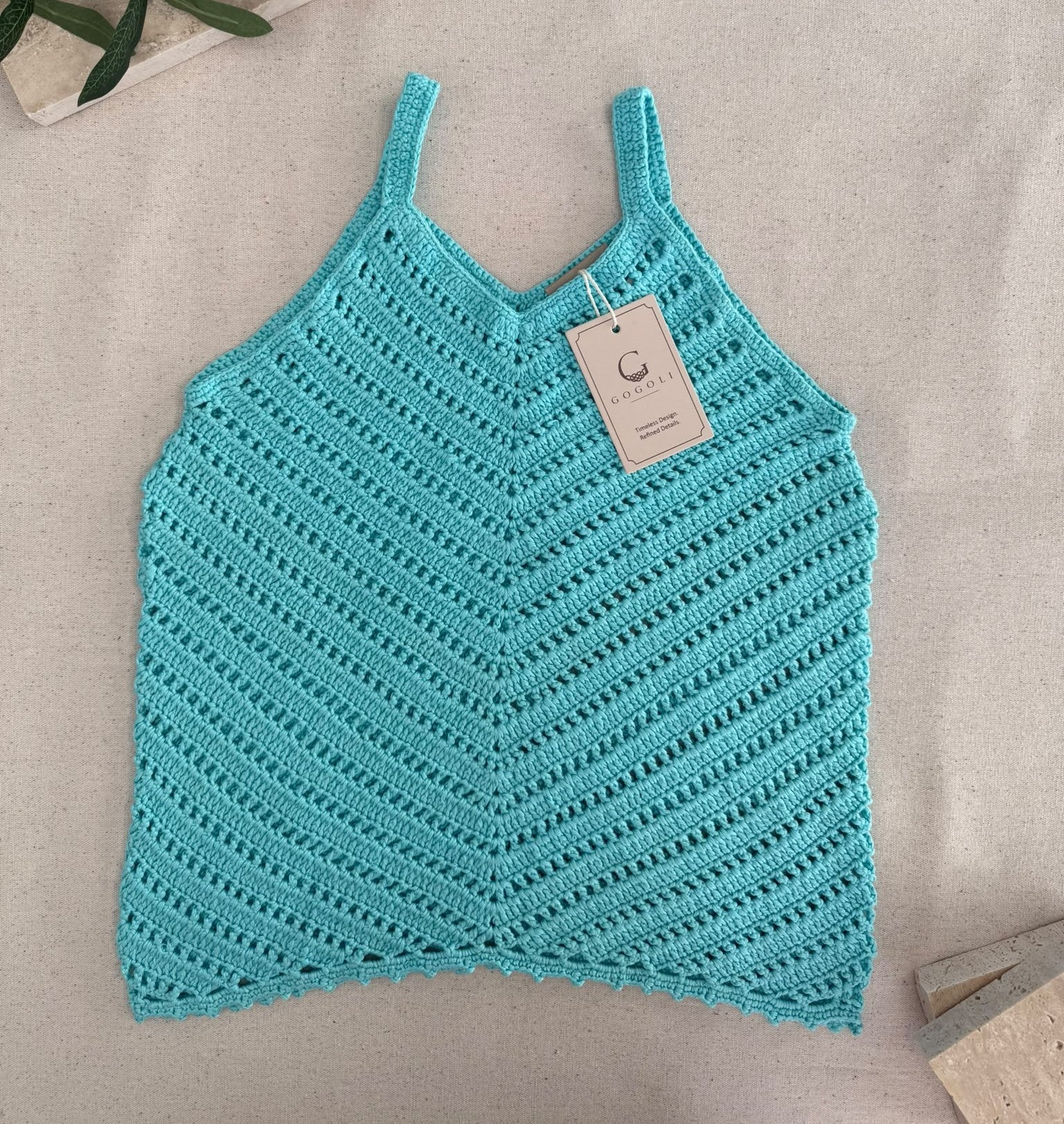 Full flat-lay view of the handmade turquoise crochet tank top showing its V-neckline, slim straps and overall shape.