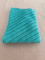 Flat-lay view of the turquoise V-neck crochet top showing its narrow straps, diagonal construction and scalloped hem.
