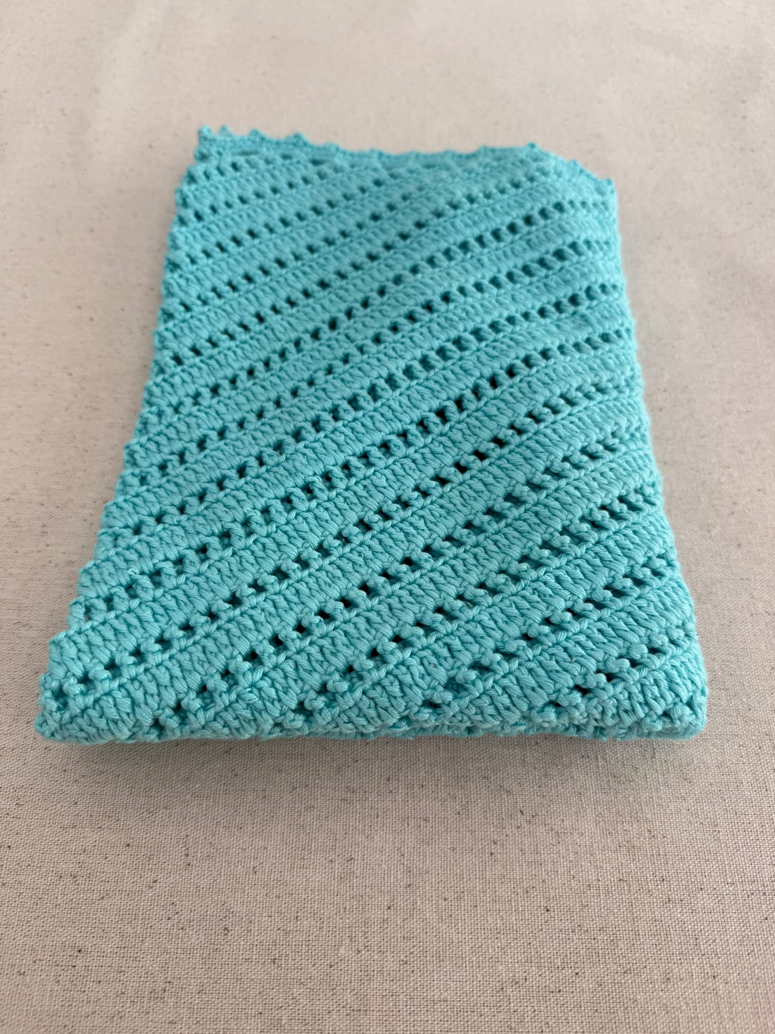 Flat-lay view of the turquoise V-neck crochet top showing its narrow straps, diagonal construction and scalloped hem.