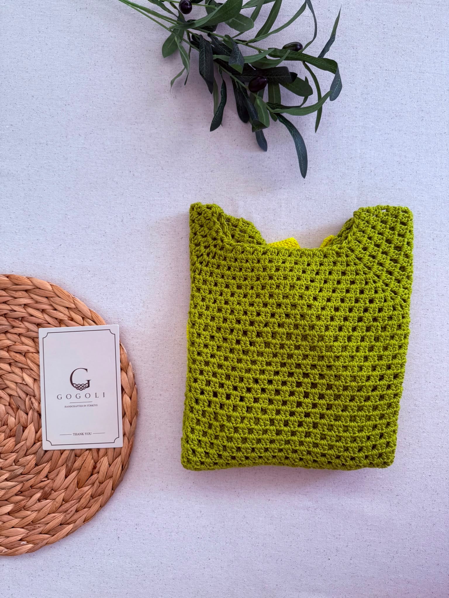 Folded front view of the two-tone green crochet jumper showing its narrow boat neckline, openwork body and contrast hem.