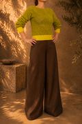 Front view of the handmade two-tone green yellow crochet jumper styled with brown wide-leg trousers, showing its narrow boat neckline and lime green trims.