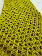 Close-up of the handmade green crochet jumper showing the repeating openwork stitch pattern and softly structured acrylic texture.