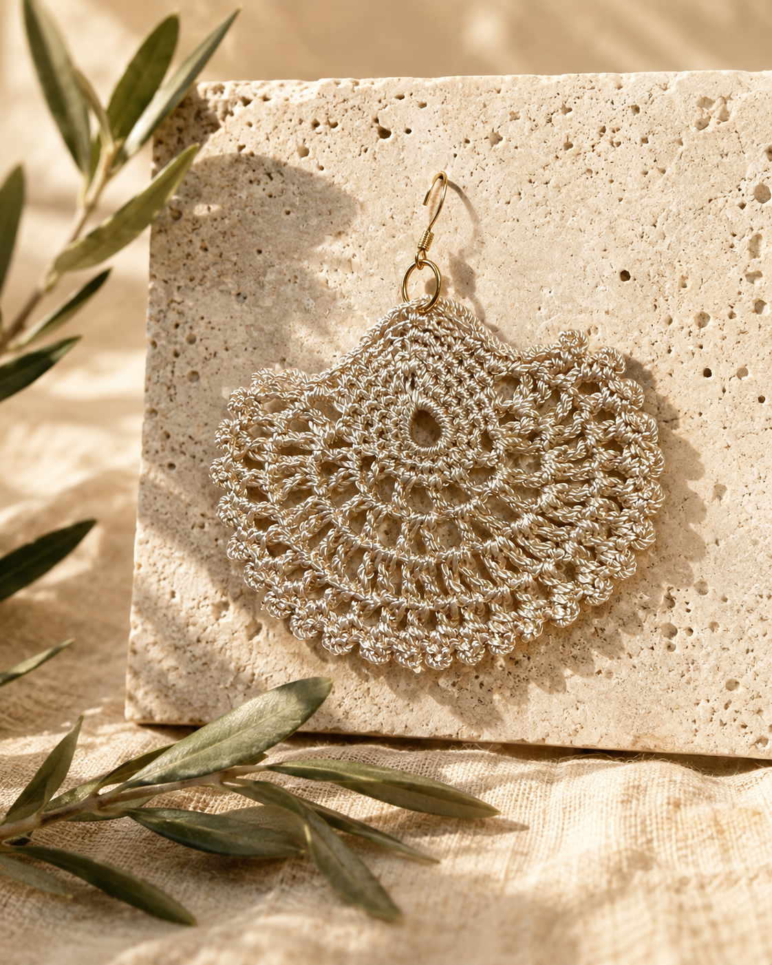 Single warm sand-beige crochet earring laid flat, showing its teardrop centre, circular openwork and scalloped edge.