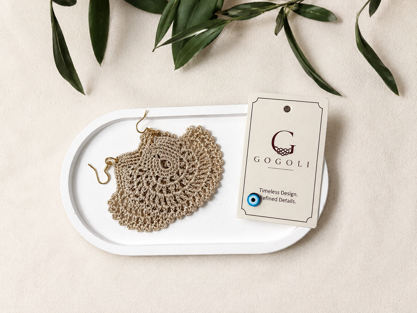 Round warm sand-beige crochet statement earring displayed on a black jewellery bust, showing its full scale and openwork surface.