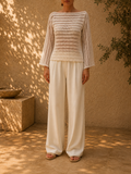 Front view of the handmade bright-white crochet blouse styled with ivory wide-leg trousers, showing its boat neckline and long openwork sleeves.