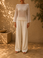 Front view of the handmade bright-white crochet blouse styled with ivory wide-leg trousers, showing its boat neckline and long openwork sleeves.