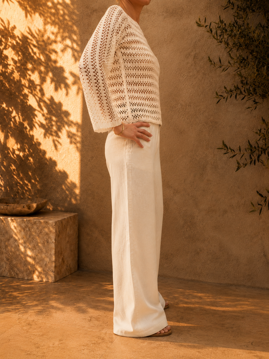 Three-quarter view of the bright-white crochet blouse highlighting its wide boat neckline, long sleeves and subtle sheen.
