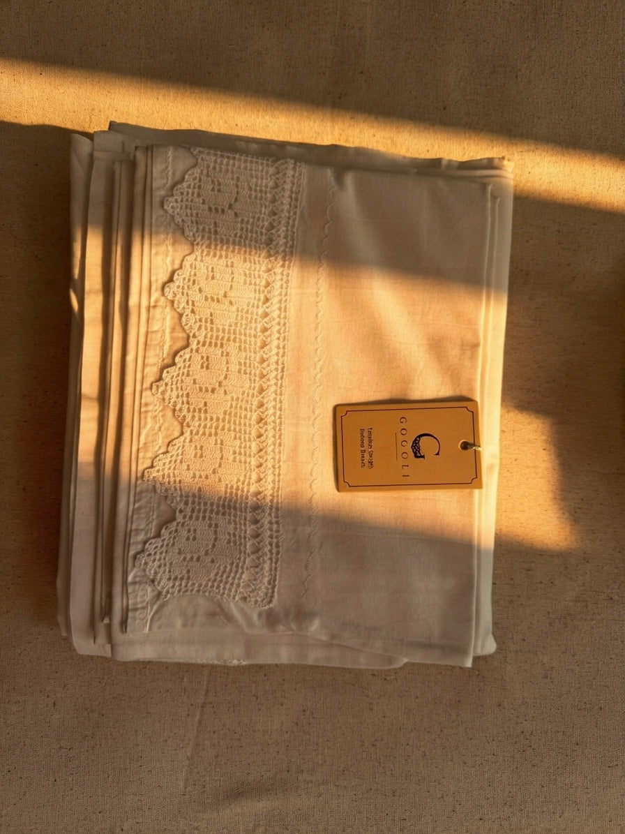 Folded white cotton bed sheet showing the handmade crochet lace stitched onto the fabric surface.