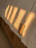 Side detail of the white cotton bed sheet showing handmade crochet lace positioned within the long edge of the fabric.