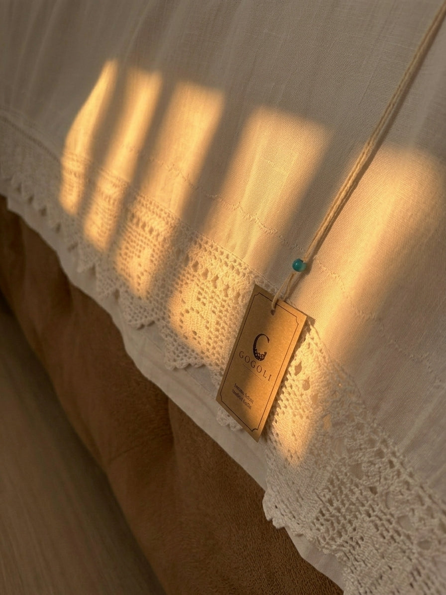 Side detail of the white cotton bed sheet showing handmade crochet lace positioned within the long edge of the fabric.