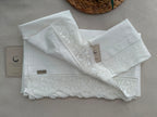 Detail view of the folded white cotton bedding set showing the handmade lace edges and soft plain-weave fabric.
