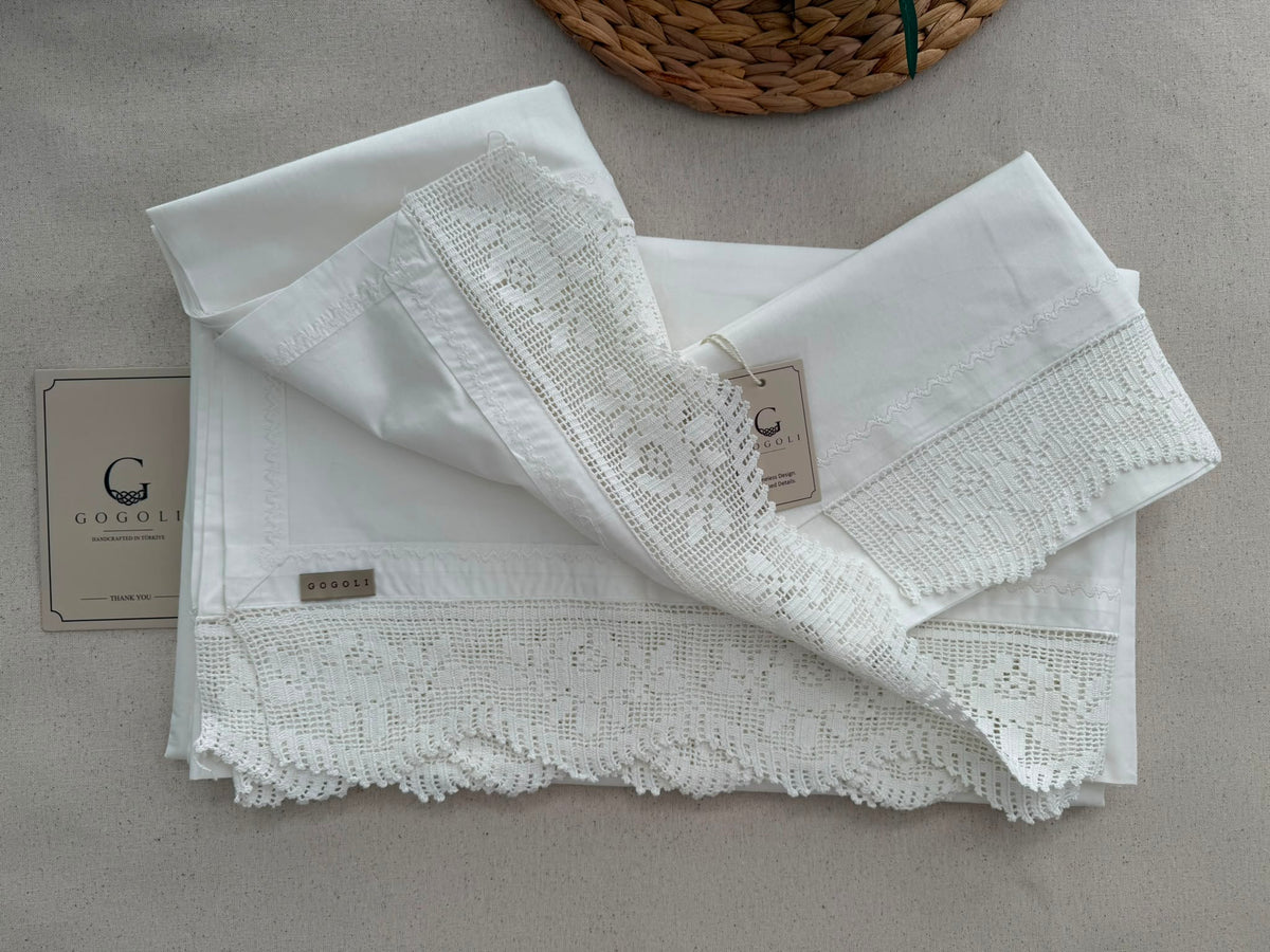 Detail view of the folded white cotton bedding set showing the handmade lace edges and soft plain-weave fabric.