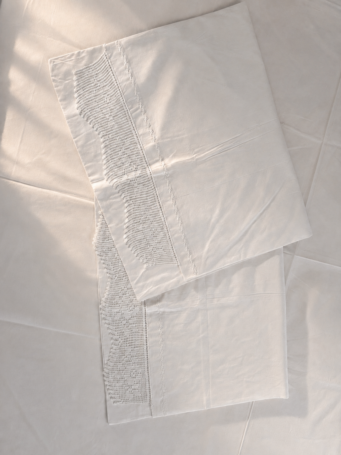 White cotton pillowcase styled on the bed with handmade crochet lace along one selected edge.