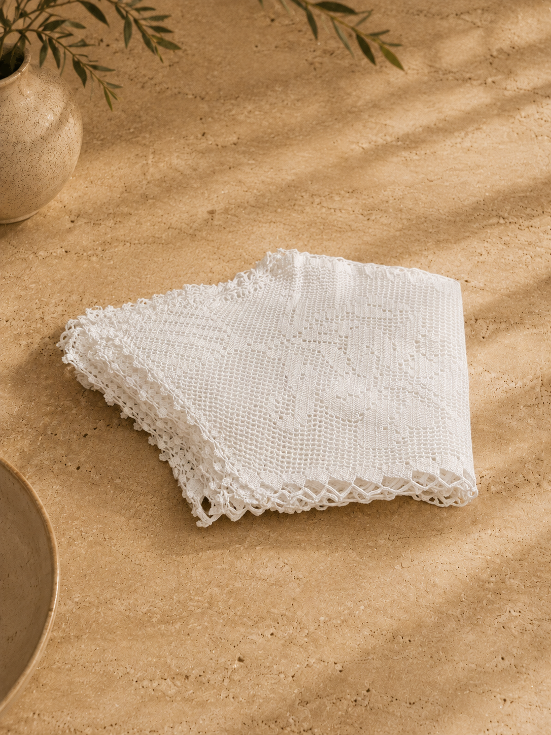 Folded detail view of the handmade white cotton table cover showing the layered crochet edges and stitch structure.