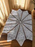 Full view of the handmade white crochet table cover showing twelve joined diamond sections forming a star-like silhouette.