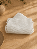 Folded view of the one-of-a-kind white cotton crochet table cover showing its handmade openwork texture.