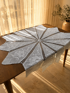 White cotton crochet table cover arranged on a wooden table, showing the radiating diamond sections and pointed outer edges.