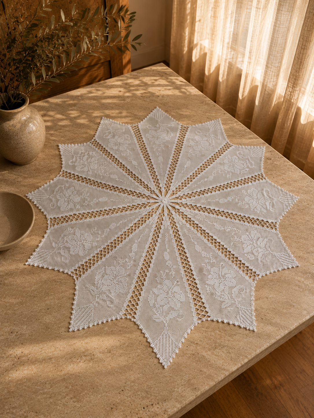 White handmade crochet tablecloth displayed across a wooden table, showing its radial twelve-section construction.